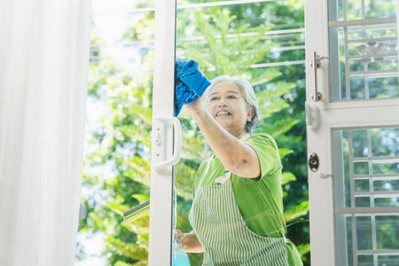 Cheerful senior woman housekeeping, Asian woman doing housework, Woman cleans the outside of a glass...