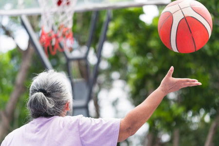 Senior Asian sportswoman shooting basketball hoop ball to court ring boardの写真素材