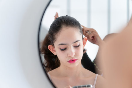 Teenage girl looks into the smartphone while her mother combs her daughter's hairの写真素材