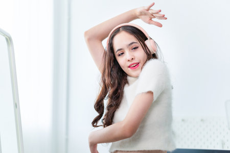 Portrait of young girl in headphones listening music and laughing while dancing in front of a mirror...