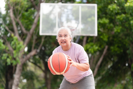 Cheerful active senior woman playing basketball in the urban outdoor basketball court, healthy life conceptsの写真素材