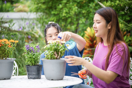 Asian group of friends take care plants in garden, spraying beautiful flowering plants with water sprayer at homeの写真素材