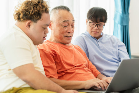 Grandfather and grandson using laptop doing a video call in living room, Asian senior man having a...