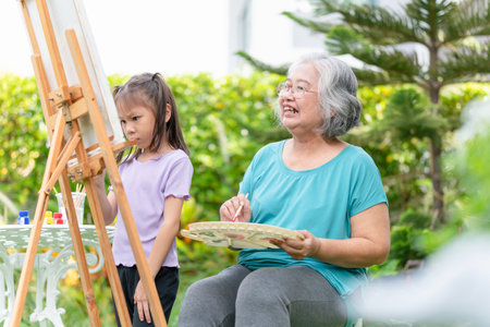 Grandmother drawing picture with kid girl in garden, Senior woman and her granddaughter play together in the gardenの写真素材