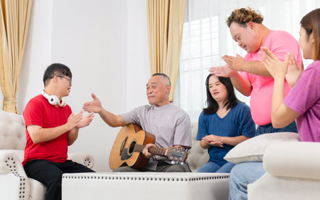 Senior man and grandchild having fun together while singing and playing the guitar in living room at homeの写真素材