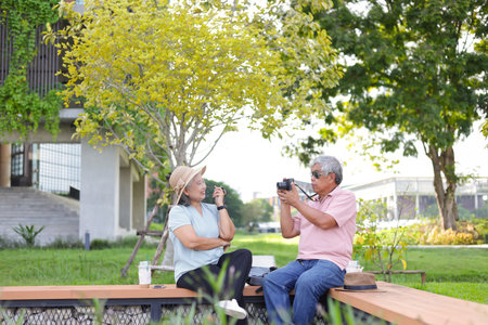 Senior couple in park, Asian senior man taking pictures of his woman sitting outdoorsの写真素材