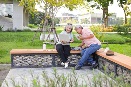 Senior couple sitting on a bench in park, Asian senior man and woman use laptop and digital tablet in parkの写真素材
