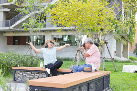 Senior couple in park, Asian senior man taking pictures of his woman sitting outdoorsの写真素材