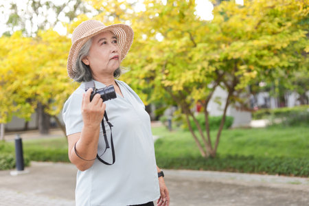 Seniur Asian woman tourist with camera at park, Female photographer holding camera outdoorの写真素材