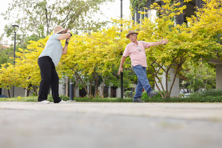 Happy Asian senior couple in park, Asian senior woman taking pictures using photo camera in parkの写真素材