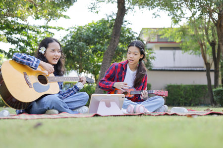 Asian kid girl and friend playing guitar in the park, Friends playing guitar on picnic in parkの写真素材