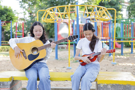 Asian kid girl and friend playing guitar in the parkの写真素材