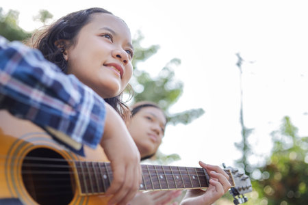 Asian kid girl and friend playing guitar in the park, Friends playing guitar on picnic in park