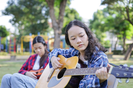 Asian kid girl and friend playing guitar in the park, Friends playing guitar on picnic in parkの写真素材