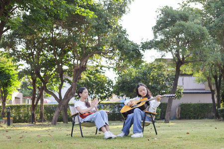 Asian kid girl learning play guitar with friend in the park, Friends playing guitar on picnic in parkの写真素材