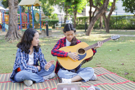 Girl and friend learning online guitar lesson in the park, Friends playing guitar on picnic in park