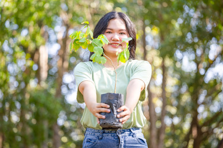 Smiling woman holding a sapling in a green park, female volunteer with a tree sapling smiling...