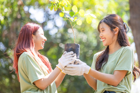 Cheerful woman holding a sapling in a green park, female volunteer team with a tree smiling cheerfully, Charity and ecology conceptsの写真素材