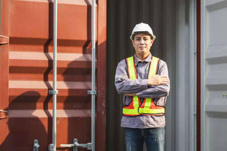 Engineer man standing with arms crossed at cargo containers, Foreman dock worker in hard hat at...
