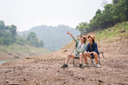 Friends Exploring Dry Riverbed with Trekking Poles, Two Young Hikers Pointing Towards Scenic Landscape, Two Girls Enjoying an Outdoor Excursionの写真素材