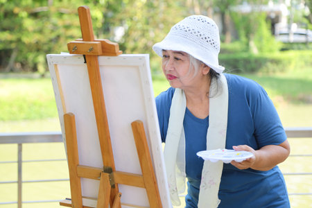 Senior Asian Woman Painting Outdoors, Creative Asian Woman with Easel in Park, Happy Elderly Female Artist Enjoying Natureの写真素材