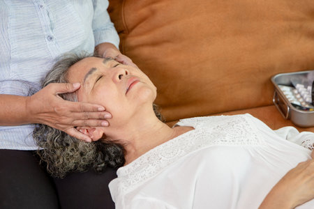 Relaxing Head and Temple Massage for Senior Woman, Elderly Asian Woman Receiving Soothing Face Massage at Home, Home Healthcare Concept for Aging Patientsの写真素材