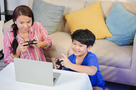 Joyful Asian Child Playing Video Games with Parent, Mom and Son Enjoying Online Gaming Together, Mother and Son Bonding Over Video Games at Homeの写真素材
