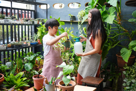Mother and Son Gardening Together at Home, Joyful Family Moment Child Helps Mom Water Plants in Urban Garden, A Young Boy and His Mother Tending to Their HousePlantsの写真素材