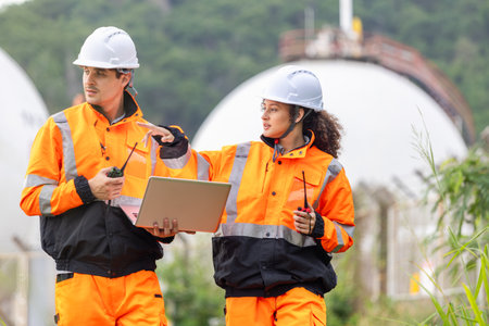 Engineers Collaborating at Industrial Site with Storage Tanks, Team of Engineers Conducting Operations at Oil Storage Field Industrial Site, Industrial Workers Communicating and Using Laptop at Siteの写真素材