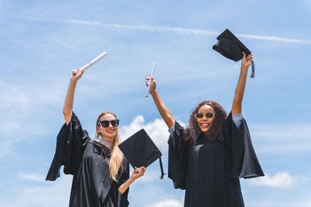 Joyful Graduates Celebrate Success Under Blue Sky, Happy Female Graduates Holding Diplomas and Caps, Achievement Unlocked Graduates Embrace Their Futureの写真素材
