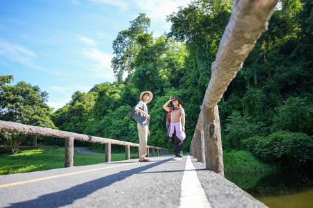 Young Friends on a Bridge in the Forest Enjoying a Hike, Backpackers on a Sunny Day in a Natural Park with a Blue Skyの写真素材