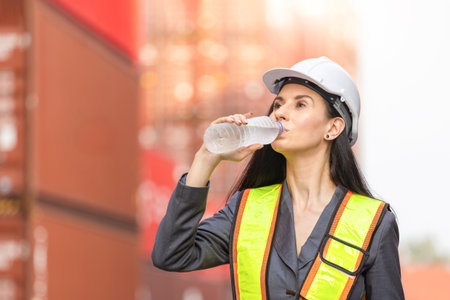 Hardworking Port Supervisors Staying Hydrated at a Shipping Terminal, Logistics Worker Taking a Water Break at a Container Yard, Female Engineers Overcoming Heat and Fatigue on the Jobの写真素材