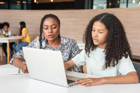 Female Teacher Assisting Student with Online Learning at Home, Mother Helping Daughter Study with Laptop for Homework Assignment, Tutor and Young Student Collaborating on Digital Education Projectの写真素材
