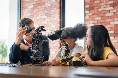 Mentor Guiding Students in Robotics and Virtual Reality (VR) Class, Man Showing Robotic Component to Girls with VR Headset, Children Learning Engineering and Programming with Adult Supervisionの写真素材