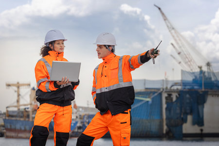 Port Engineers in Safety Gear Using Digital Devices to Plan Shipping Operations at Dockside, Man and Woman Manager Discussing Cargo Logistics Next to Ship and Craneの写真素材