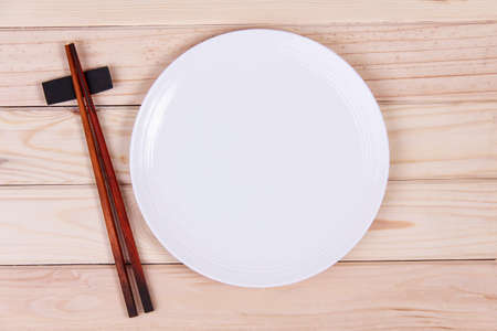 Empty white plate and sushi chopsticks on wood backgroundの写真素材