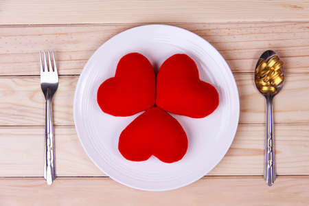 concept red heart on plate with body tonic on spoon and fork on wood background.Health care yourself should be done.の写真素材