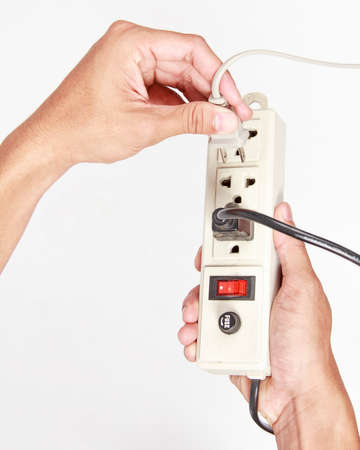Man's hand inserting an electrical plug into multiple socket bar on white background.