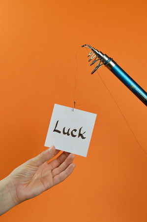 A hand grabbing a piece of paper with the word LUCK written on dangling from a fishing pole