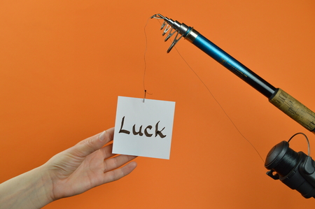 A hand grabbing a piece of paper with the word LUCK written on dangling from a fishing poleの写真素材