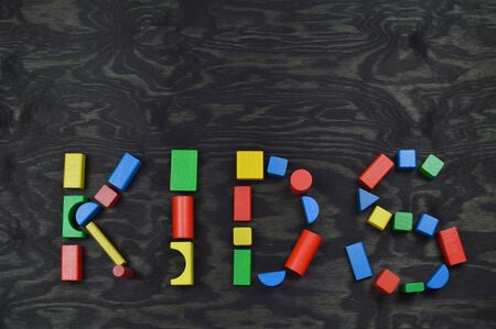 The word KIDS out of colorful wooden toy blocks on black wooden background with copyspace aboveの写真素材