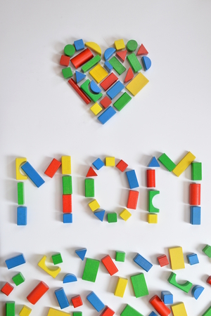 Colorful wooden toy blocks lettering the word MOM and a heart on white backgroundの写真素材