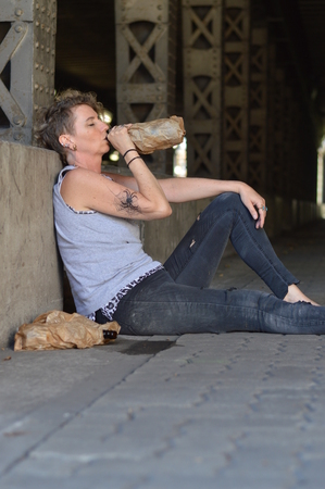 A punk woman drinking alcohol out of a bottle in a brown paper bagの写真素材