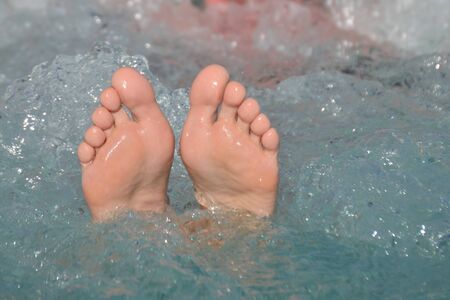 Female bare feet out of bubbling water in a hot tub outdoors in summertime in vacation