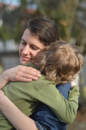 Happy mother holding little child in her arms with love in a garden outdoors in summertimeの写真素材