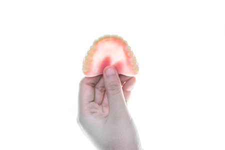 denture in hand on white background