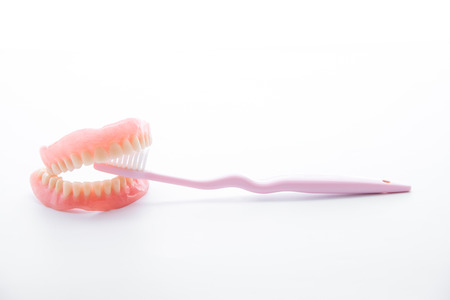 Acrylic dentures with toothbrush on white background