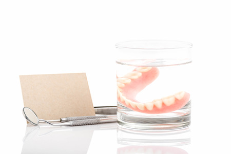 Close up of dentures in glass of water and dental tool with notice paper on white backgroundaの写真素材