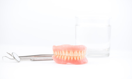 Photo of full dentures with glass of water and dental mirror on white background