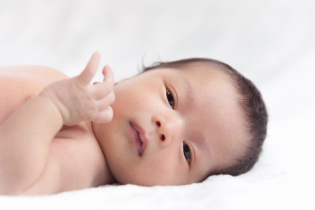 Cute baby child lying in bed with white blanketの写真素材